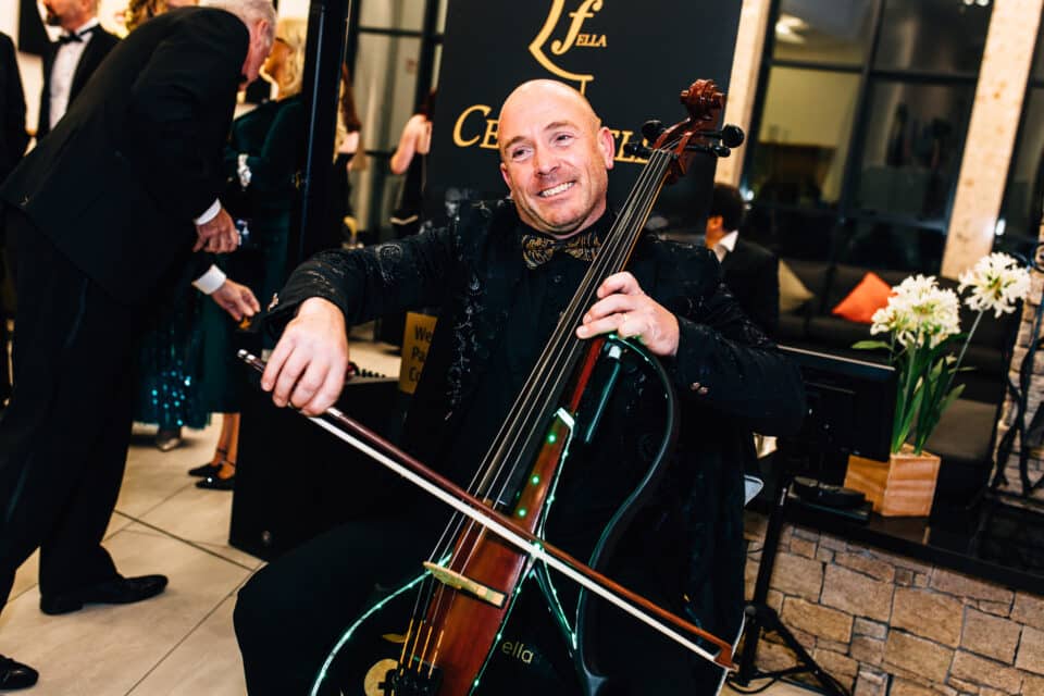 Man smiling while playing an electronic cello at a formal event.