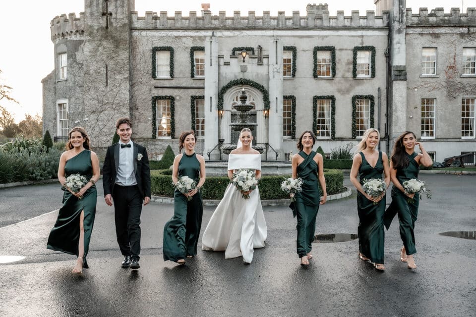 Bride with groom and bridesmaids in emerald dresses walking outside Bellingham Castle.
