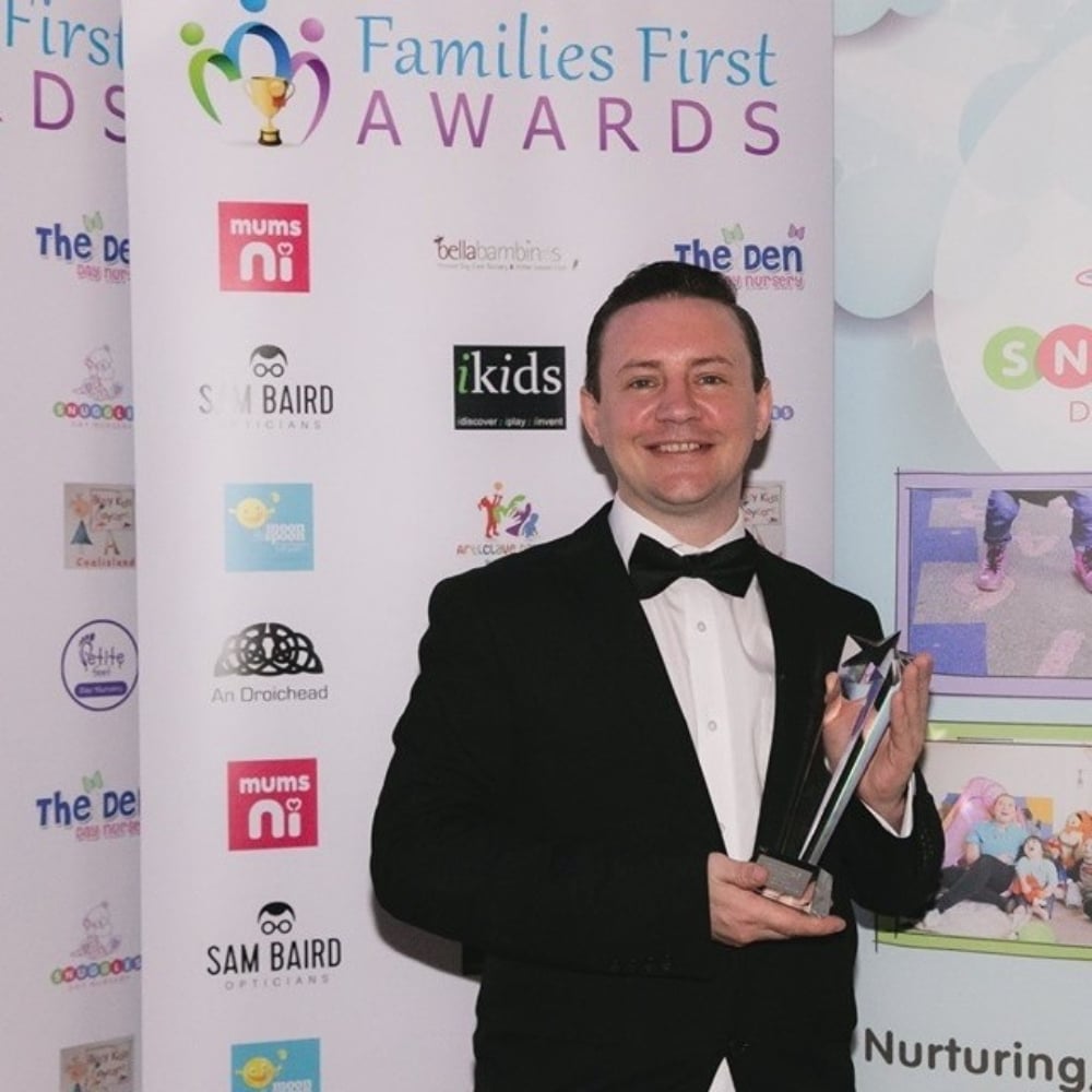 Man in a black tuxedo holding an award at the Families First Awards event.