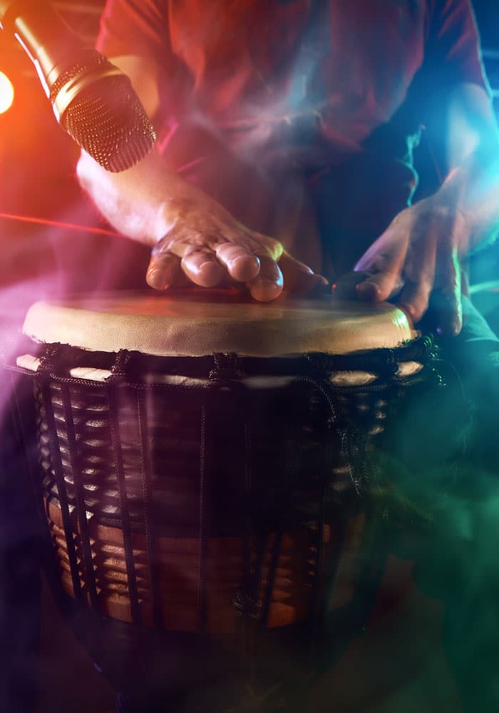Musician playing bongos with colorful stage lighting and microphone.