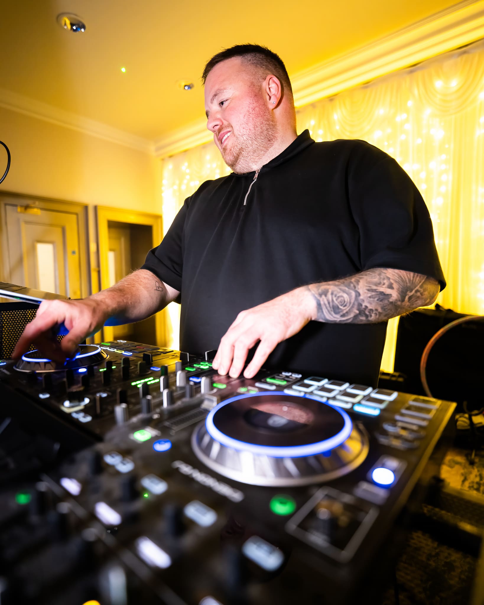 DJ performing with turntables and mixer at an indoor event, surrounded by warm lighting.