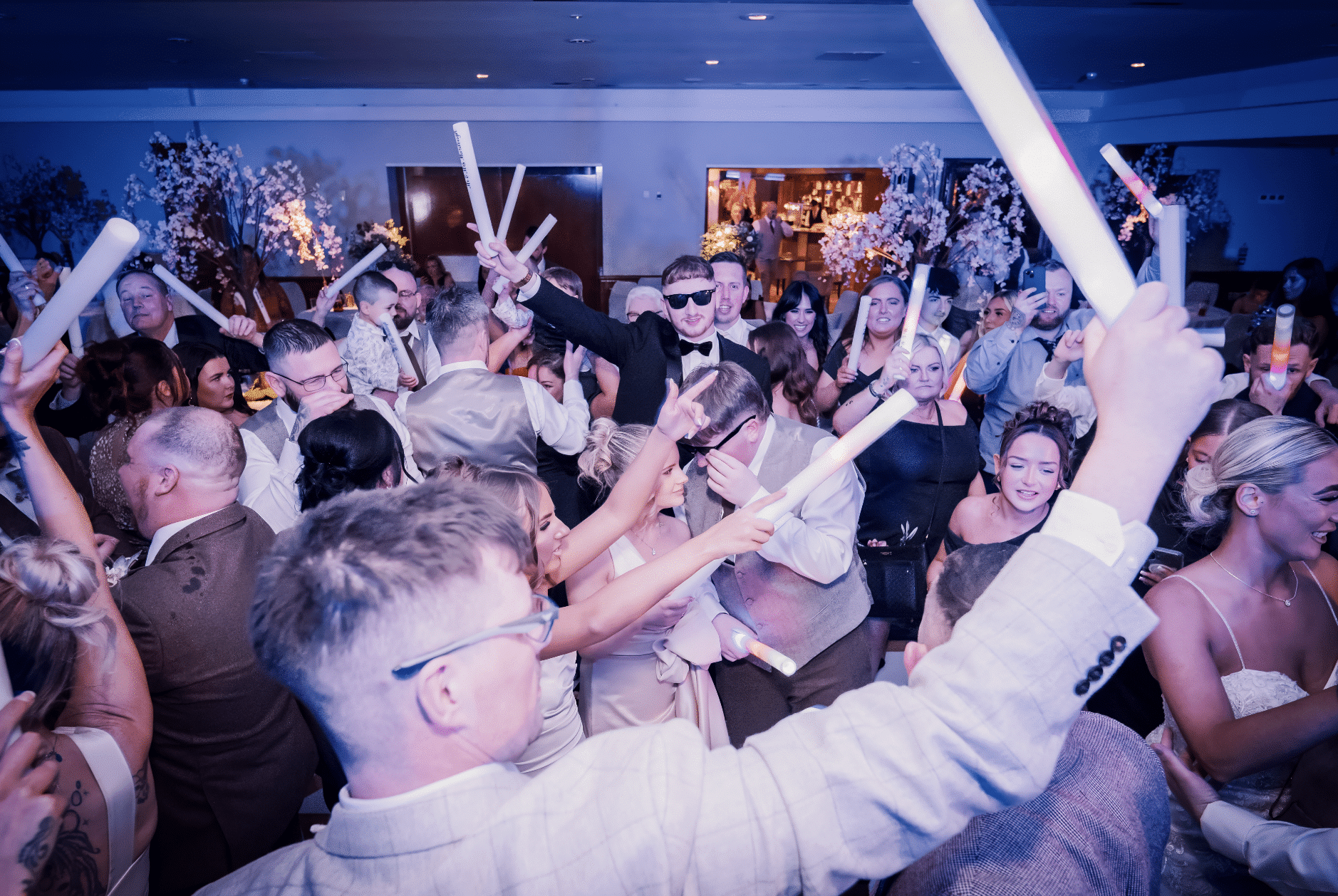 People celebrating at a party with glow sticks, dressed in formal attire.